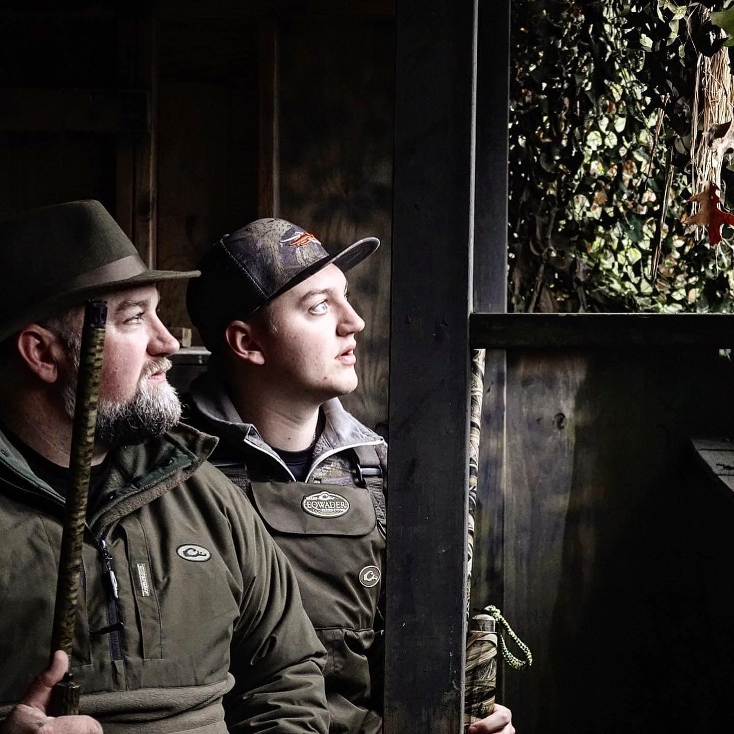 Hunters in camouflage gear positioned in a dark hunting blind.