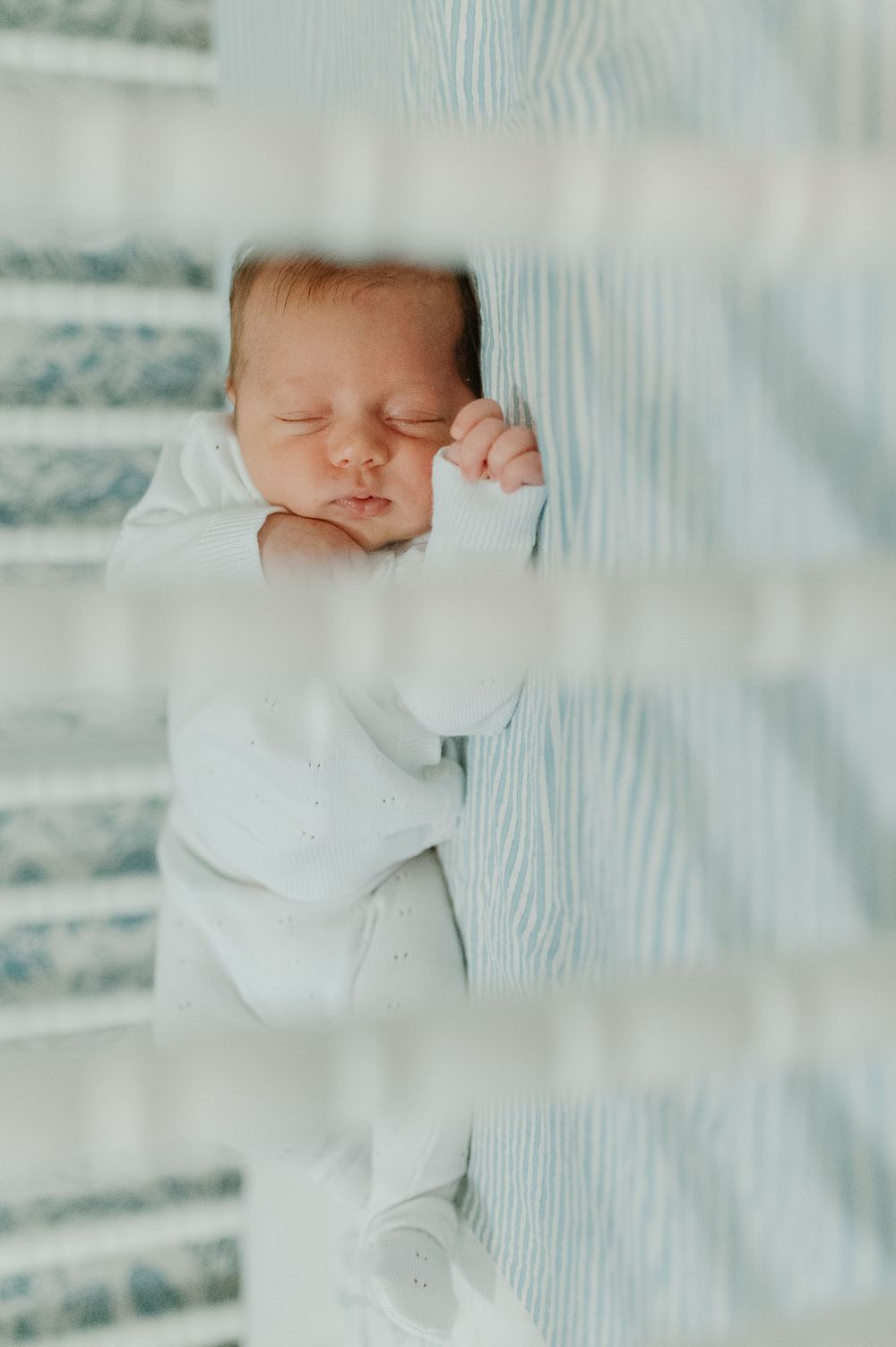 A sleeping newborn baby in white clothing rests peacefully against soft blue fabric.