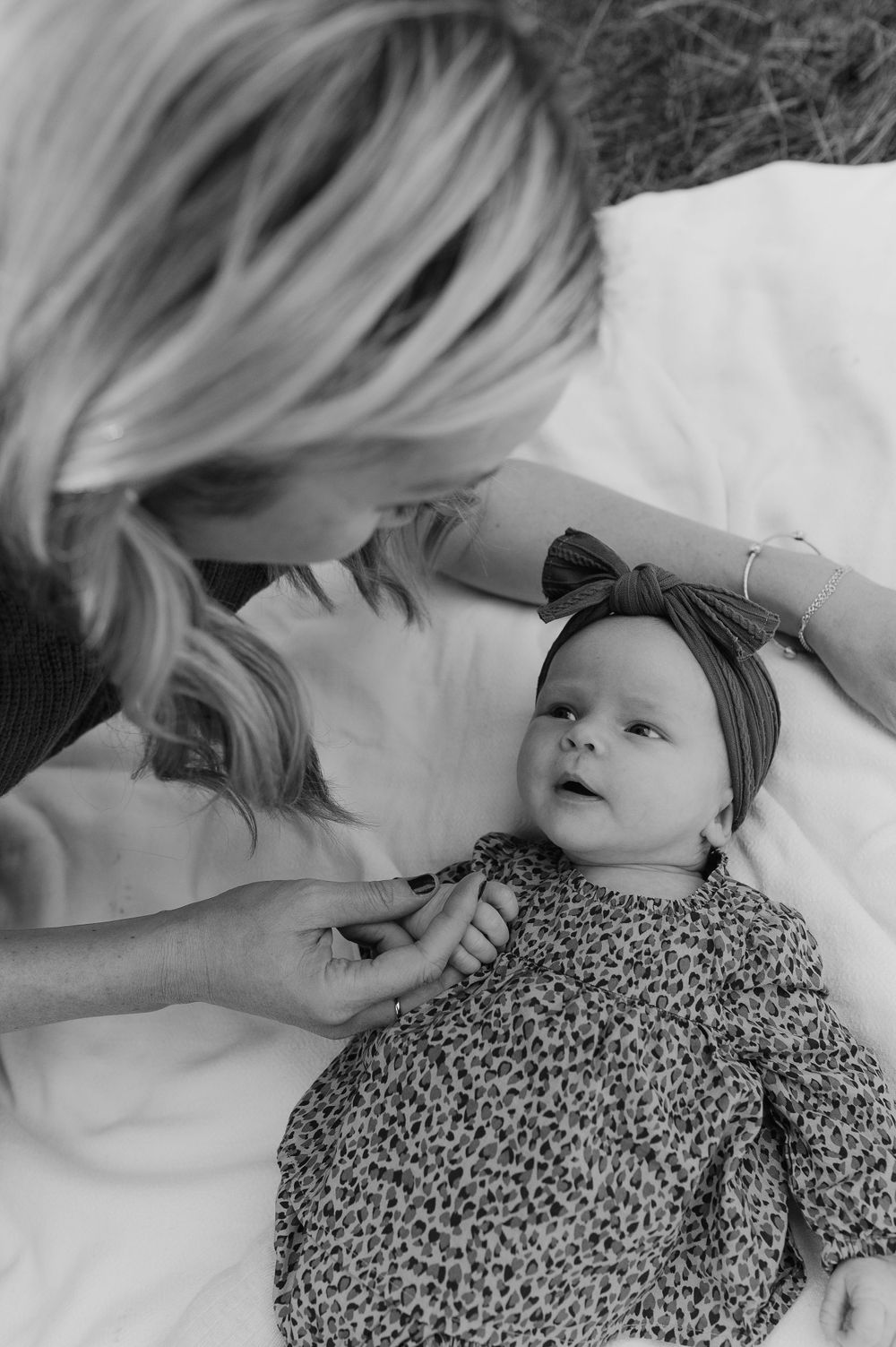 A black and white portrait of gentle interaction with a baby wearing a patterned outfit and bow.