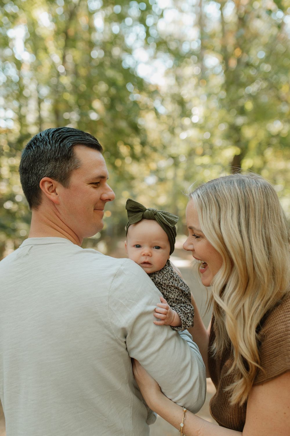 A candid family portrait in a sunlit forest showing joyful interaction and laughter.