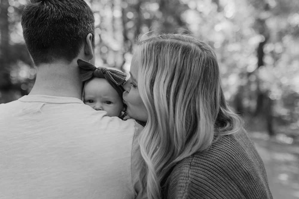 A black and white outdoor family moment capturing tender affection in a natural setting.