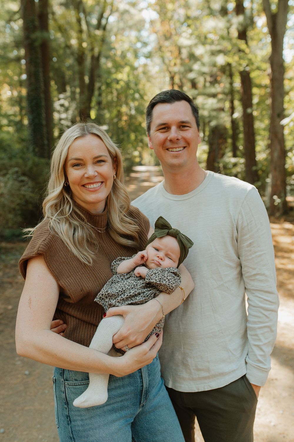 A sunny outdoor family portrait on a wooded trail capturing a happy moment together.