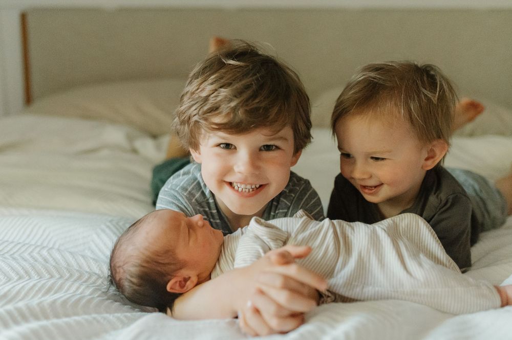 Three siblings sharing a tender moment together on white bedding.