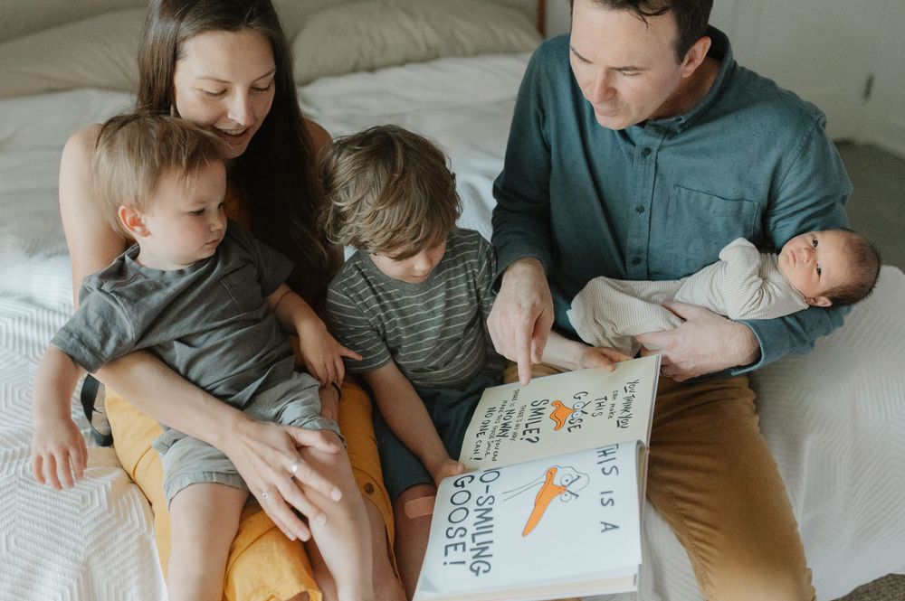 Family reading a storybook together while relaxing on bed.