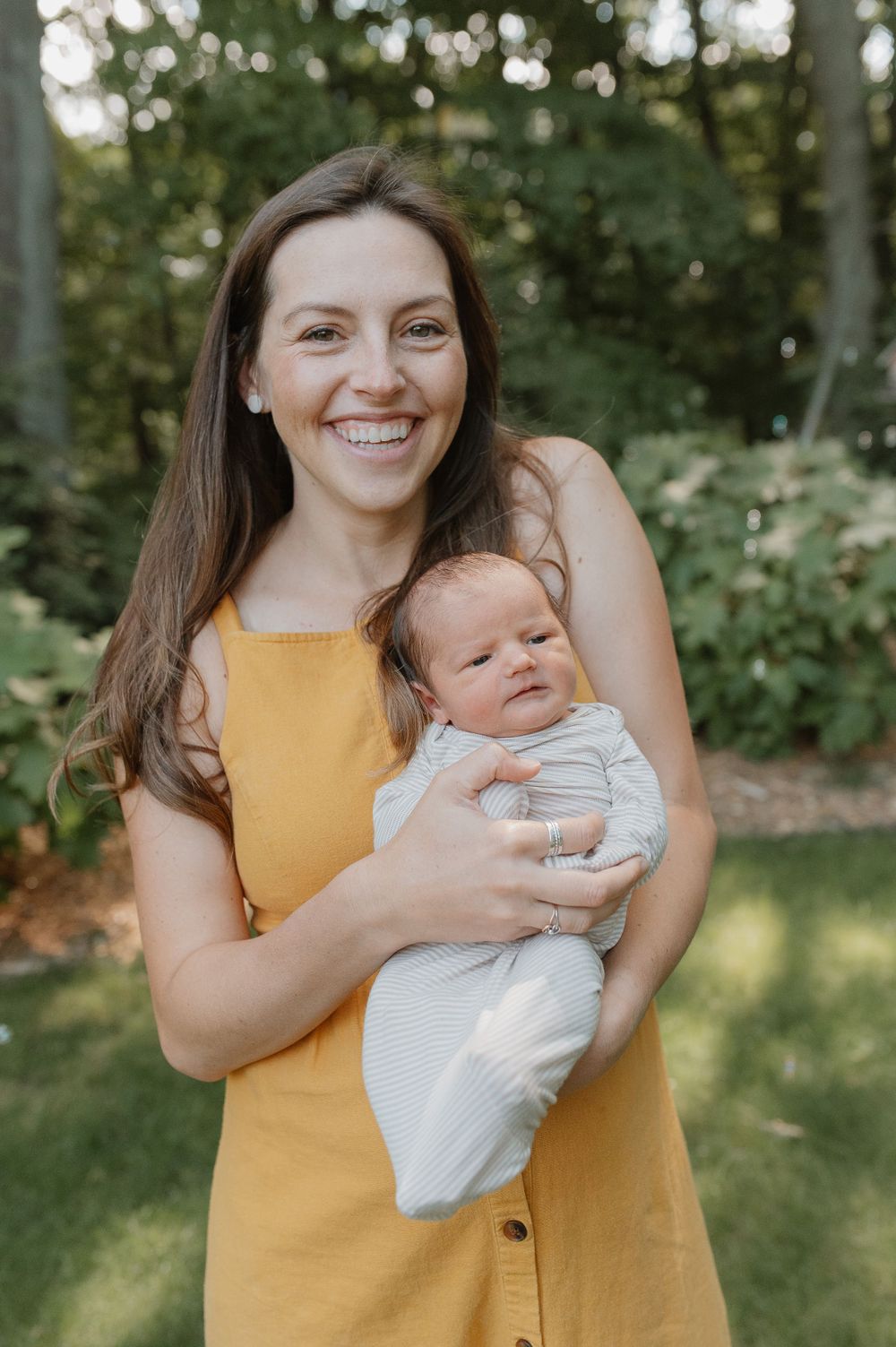 Outdoor portrait of woman in yellow dress holding baby in white outfit.
