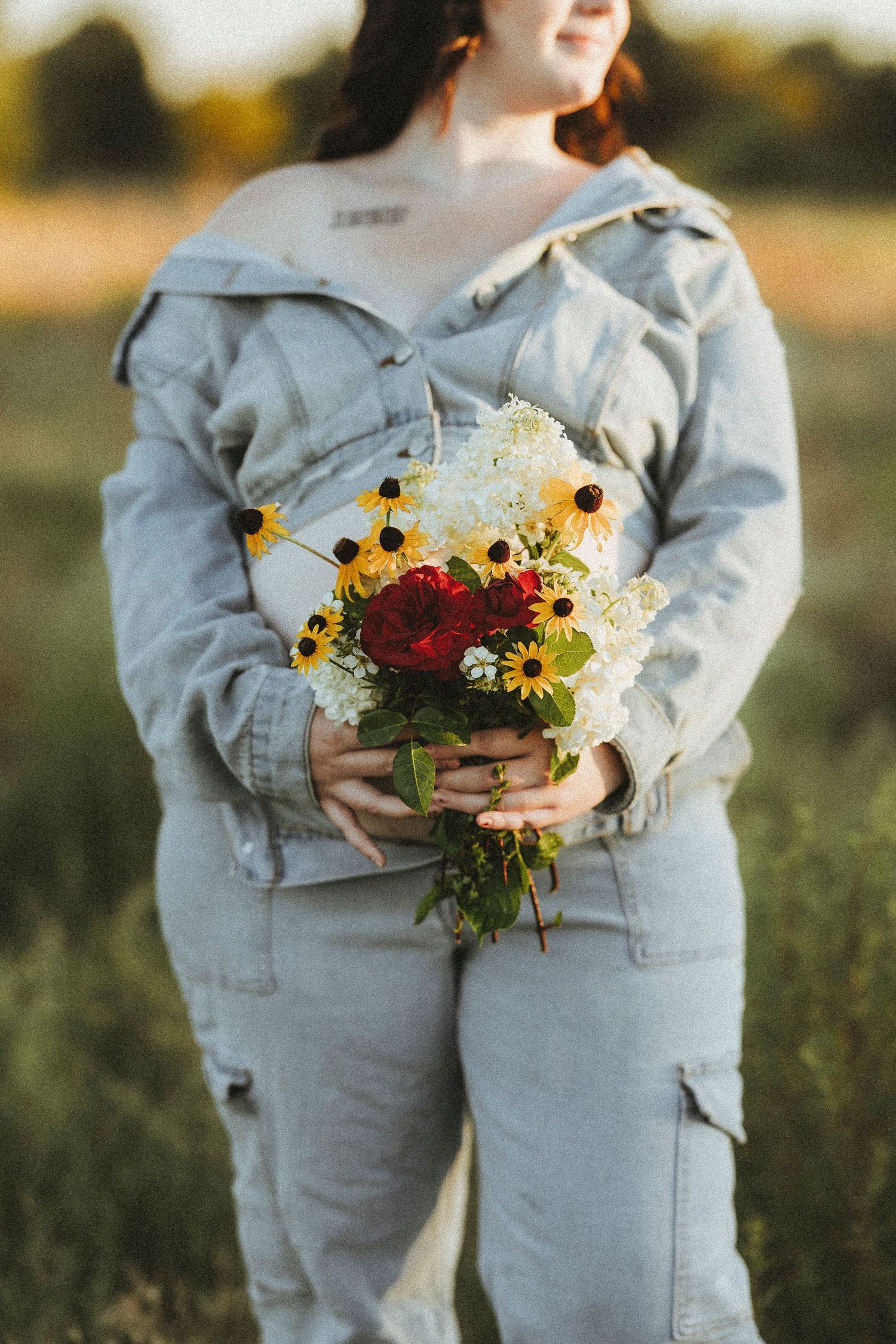 Maternity photos of the mom to be holding a bouquet of roses and sunflowers over her baby bump