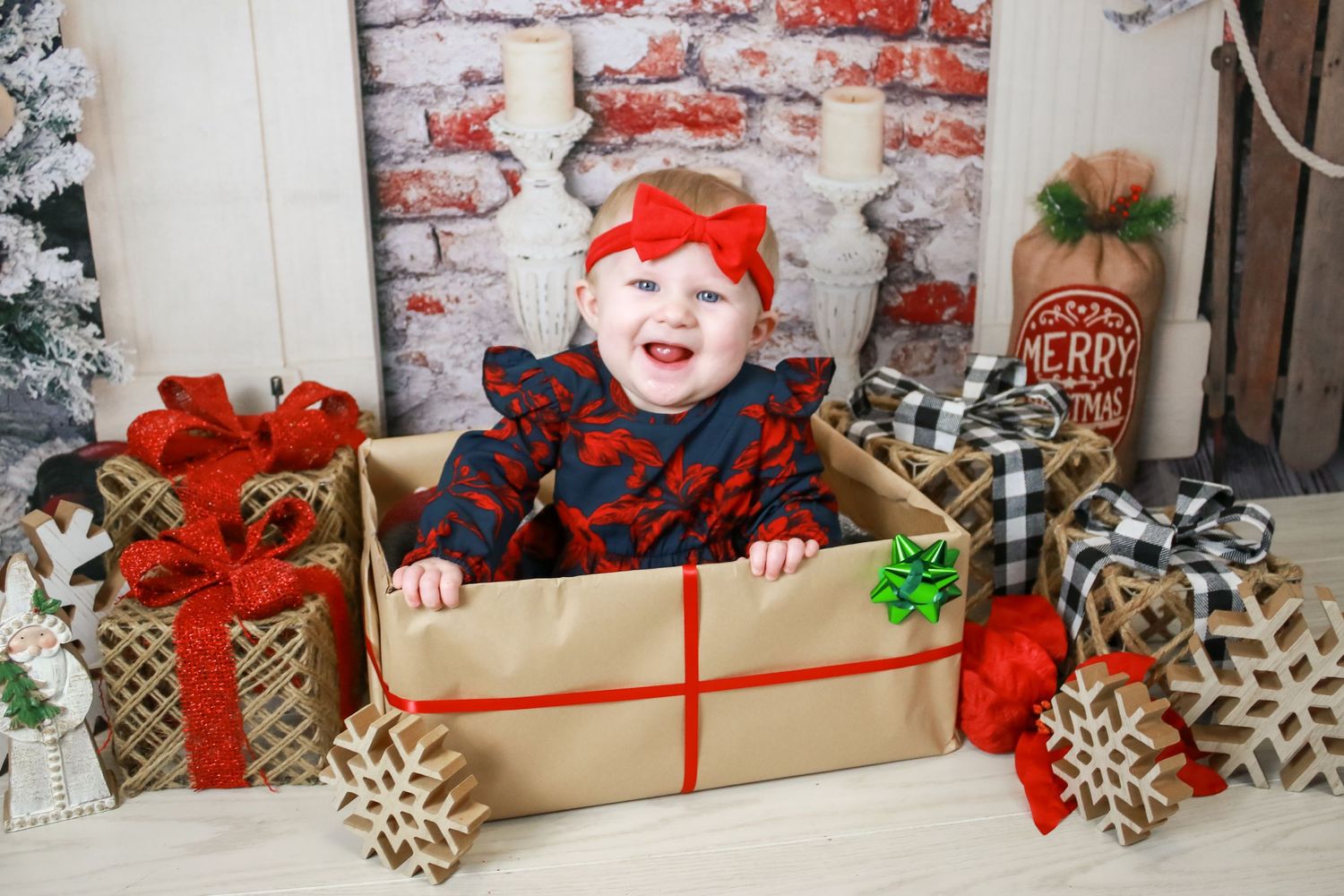 Holiday photo setup with wrapped presents and snowflake decorations against brick wall backdrop.