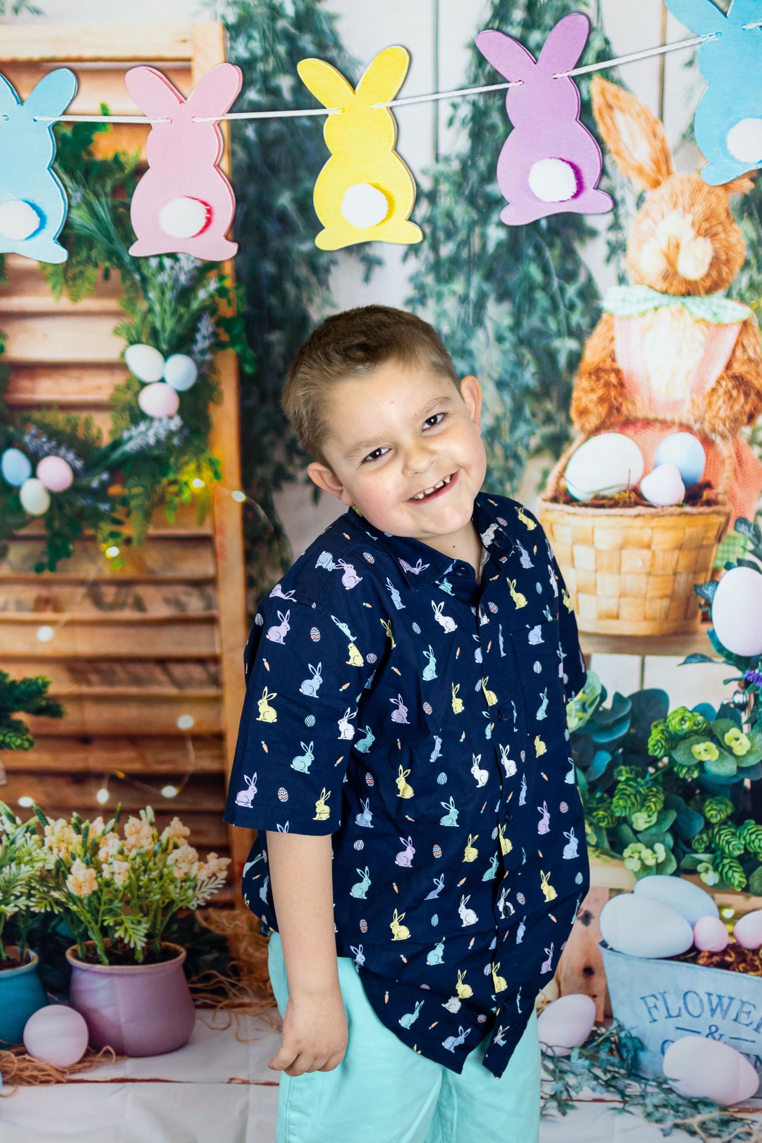 Child in navy bunny print outfit posing against Easter backdrop with pastel butterflies.