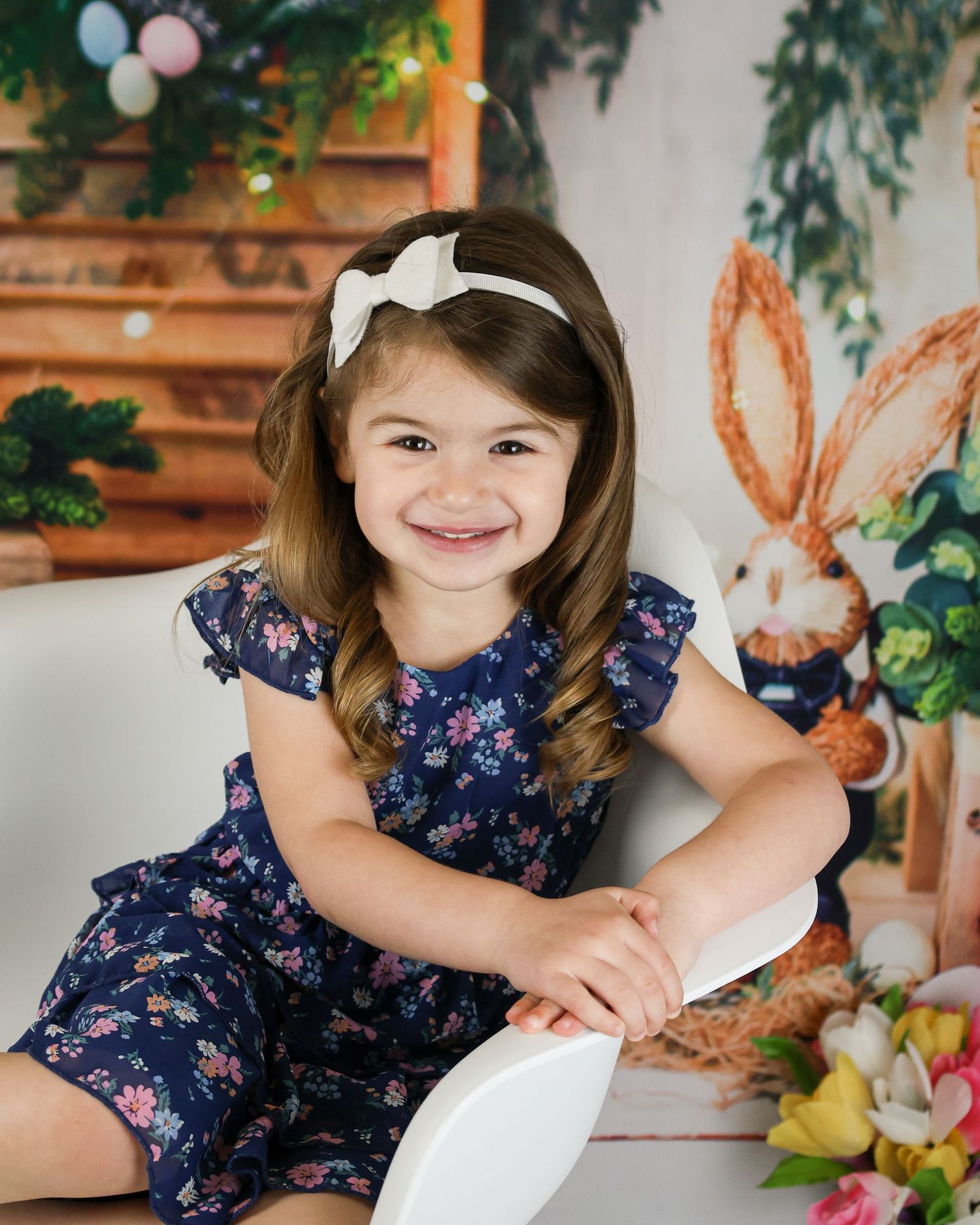 Young girl in navy floral dress posing in front of Easter-themed backdrop with balloons and decorations.