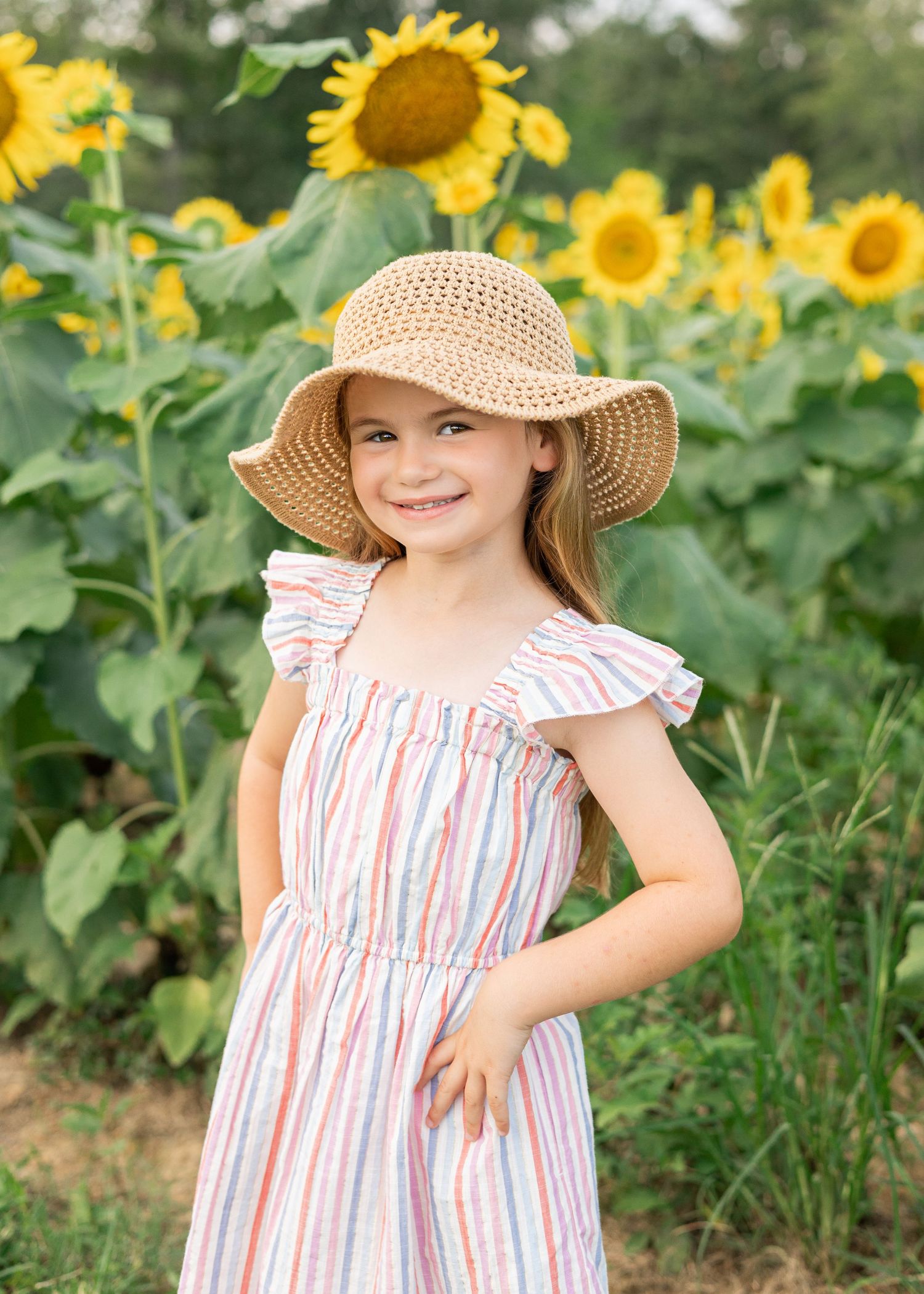 Young person in striped dress poses playfully among blooming sunflowers.