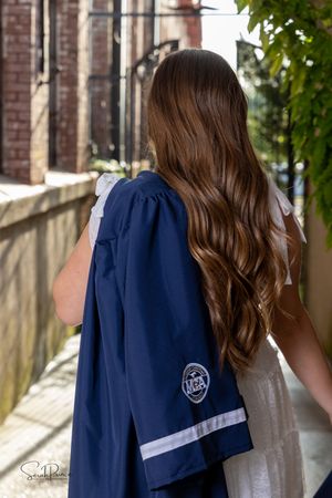 Long wavy brown hair cascading down a person's back wearing a navy blue jacket with white stripes and emblem.