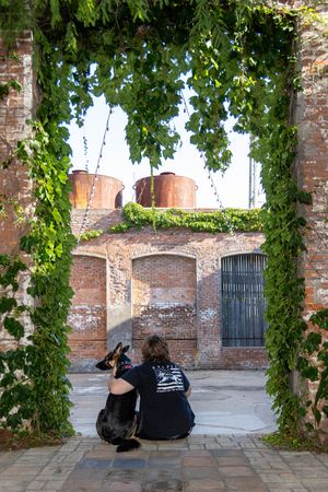 People sitting against a rustic brick wall under green leafy vines in an outdoor courtyard setting.
