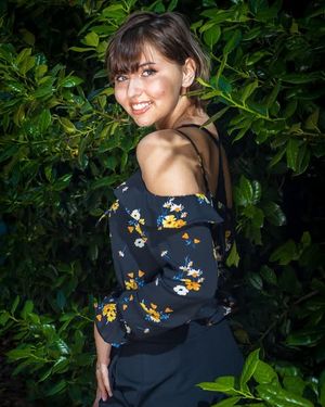 Person wearing a black butterfly print top poses against lush green foliage background in outdoor photoshoot series.
