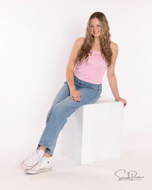 Person in pink top and blue jeans sits casually against white background in studio photoshoot.