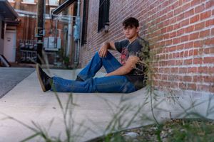 Person in blue jeans and jacket relaxes on outdoor steps against red brick wall.