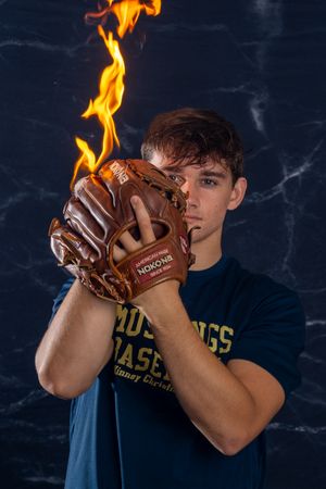 A dramatic sports photo showing a baseball glove with flames coming off it against a dark background.