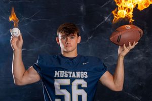 Football players in blue Mustangs jerseys pose with trophies and awards for a team photo.