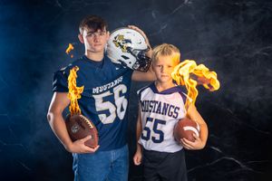 Sports themed photo shoot with navy blue jerseys and dramatic dark background lighting.
