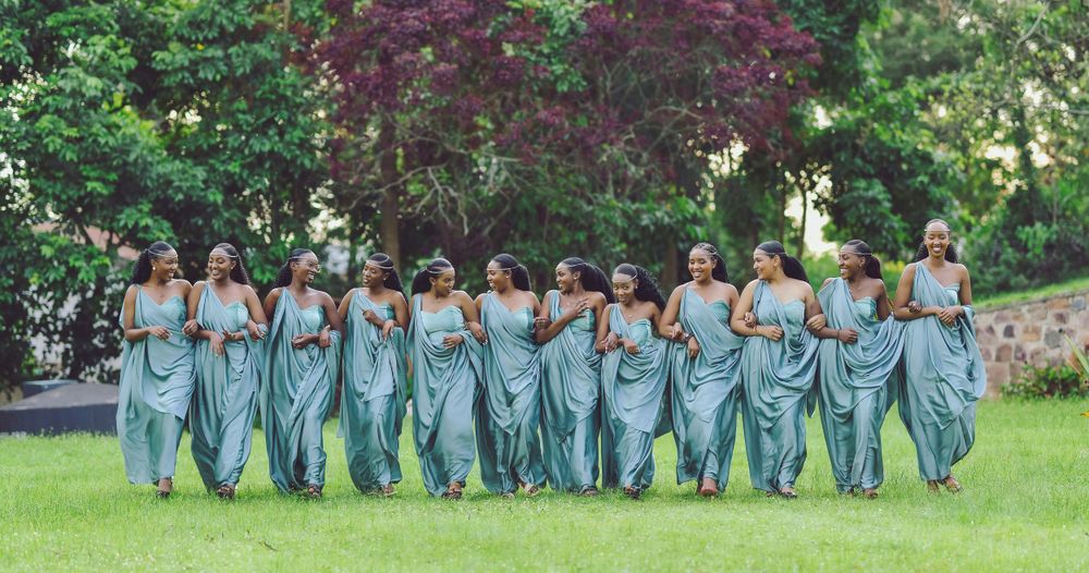 Row of bridesmaids in matching sage green dresses pose together in garden setting.