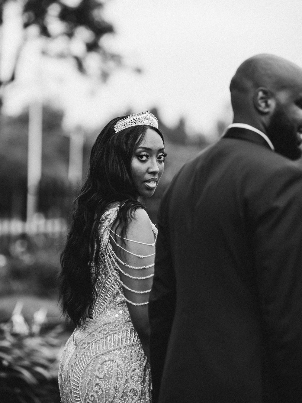 Glamorous bride in beaded gown and tiara glances over shoulder during wedding photoshoot.