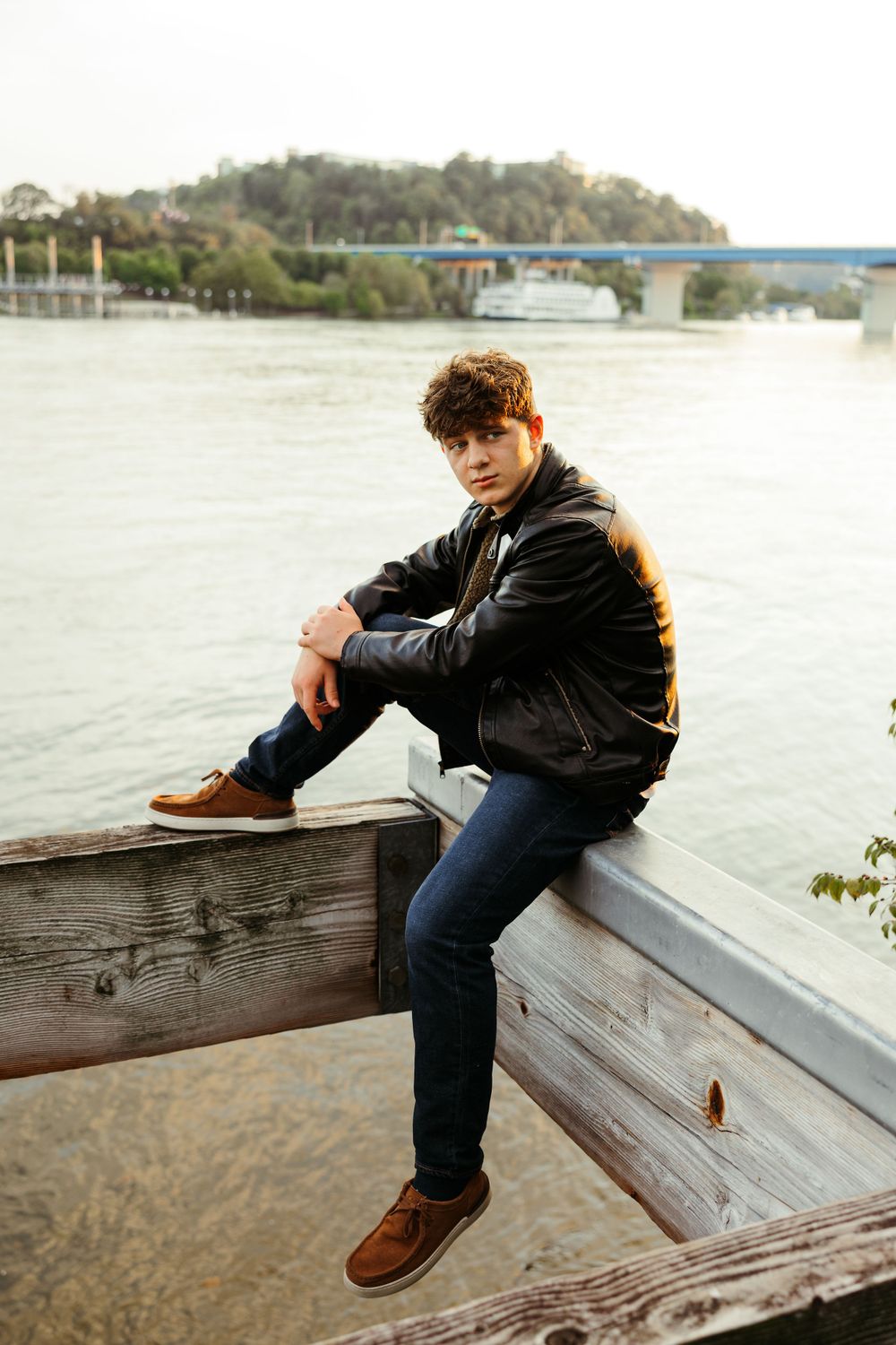 A casual portrait by the waterfront with a bridge visible in the background.