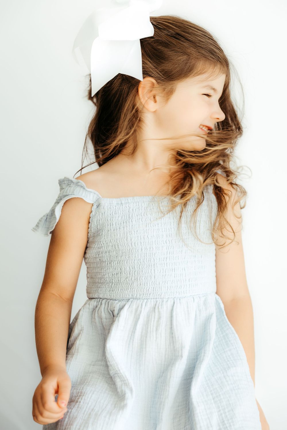 Young child in white smocked dress spins and dances with hair flowing in a series of dynamic movement shots.