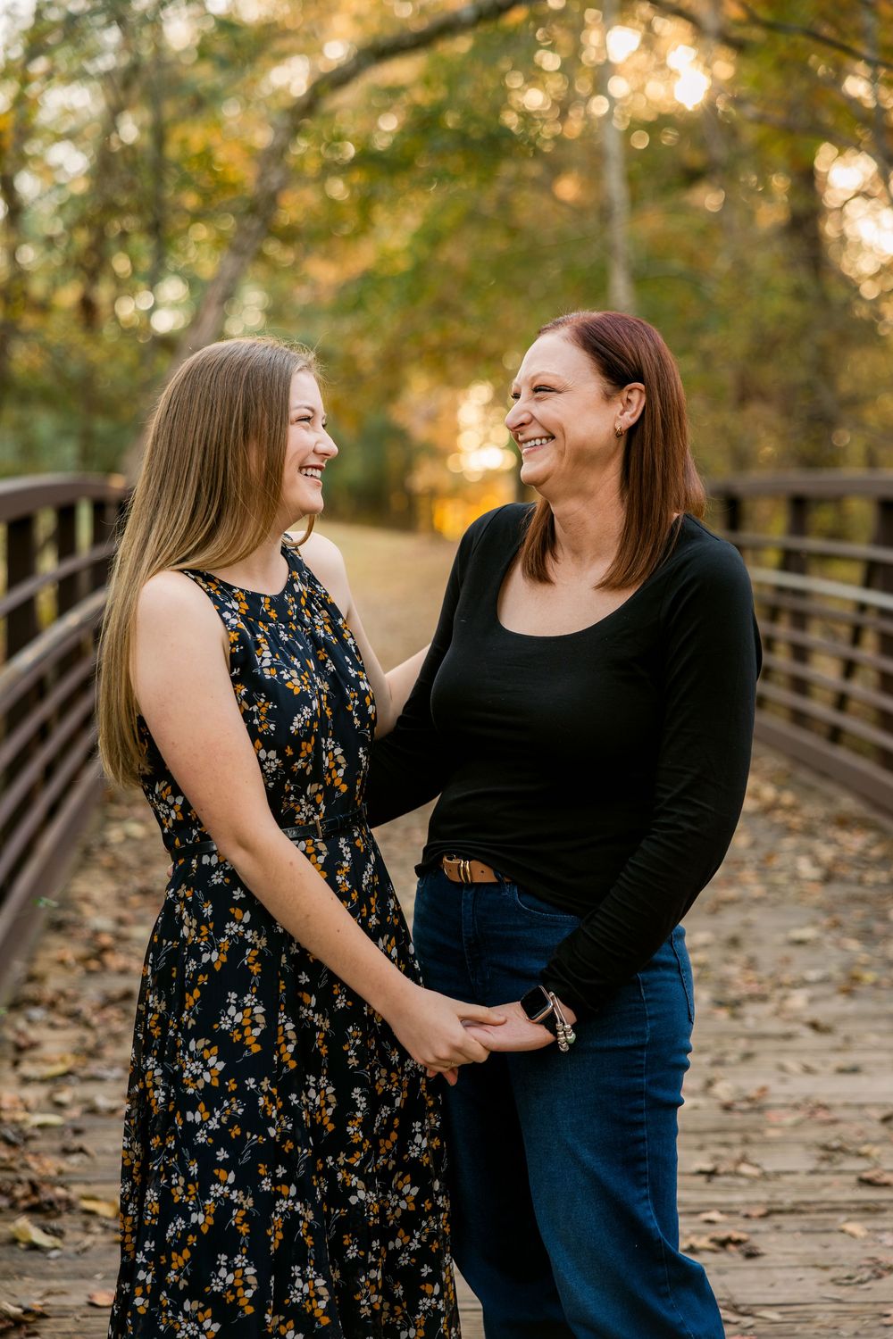 Two people sharing a joyful moment together while standing on a wooden bridge surrounded by autumn trees.