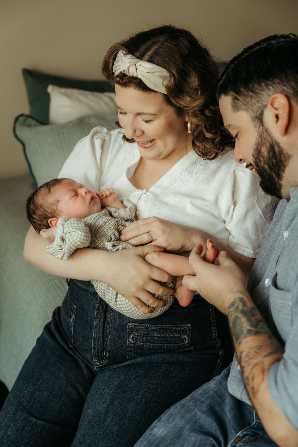 A tender family moment as parents lovingly gaze at their newborn baby while sitting together on a couch.