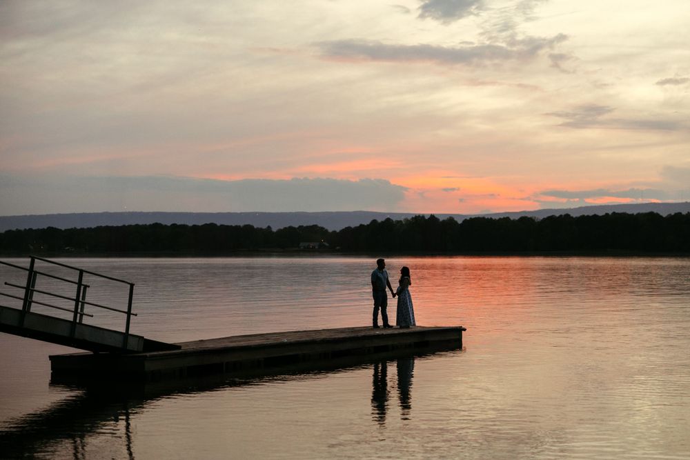 Silhouette of two people standing on dock during colorful sunset over lake.