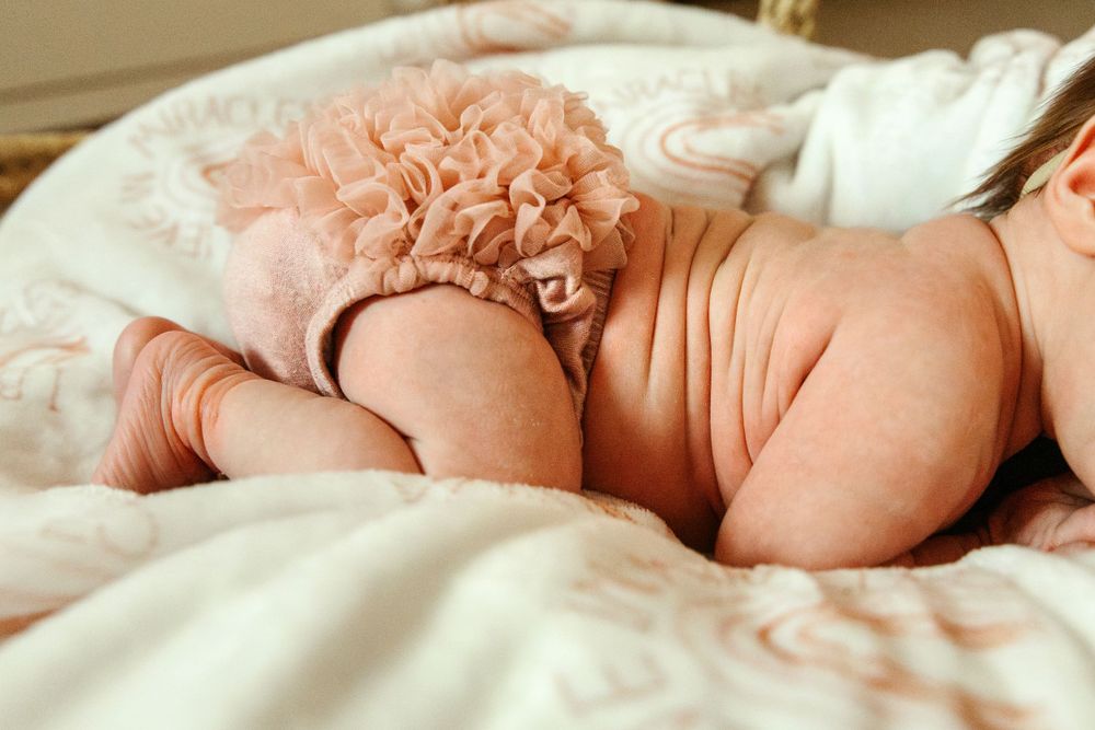 Sleeping newborn wearing pink tulle diaper cover on white bedding.