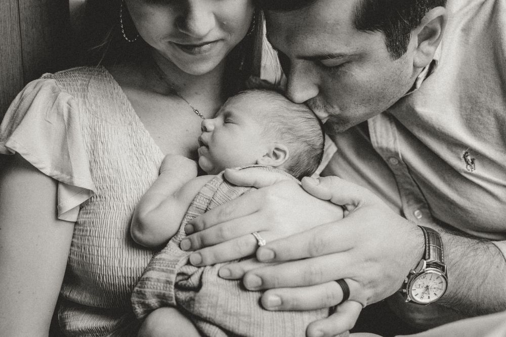 Parents sharing tender moment with their newborn baby in black and white photography.