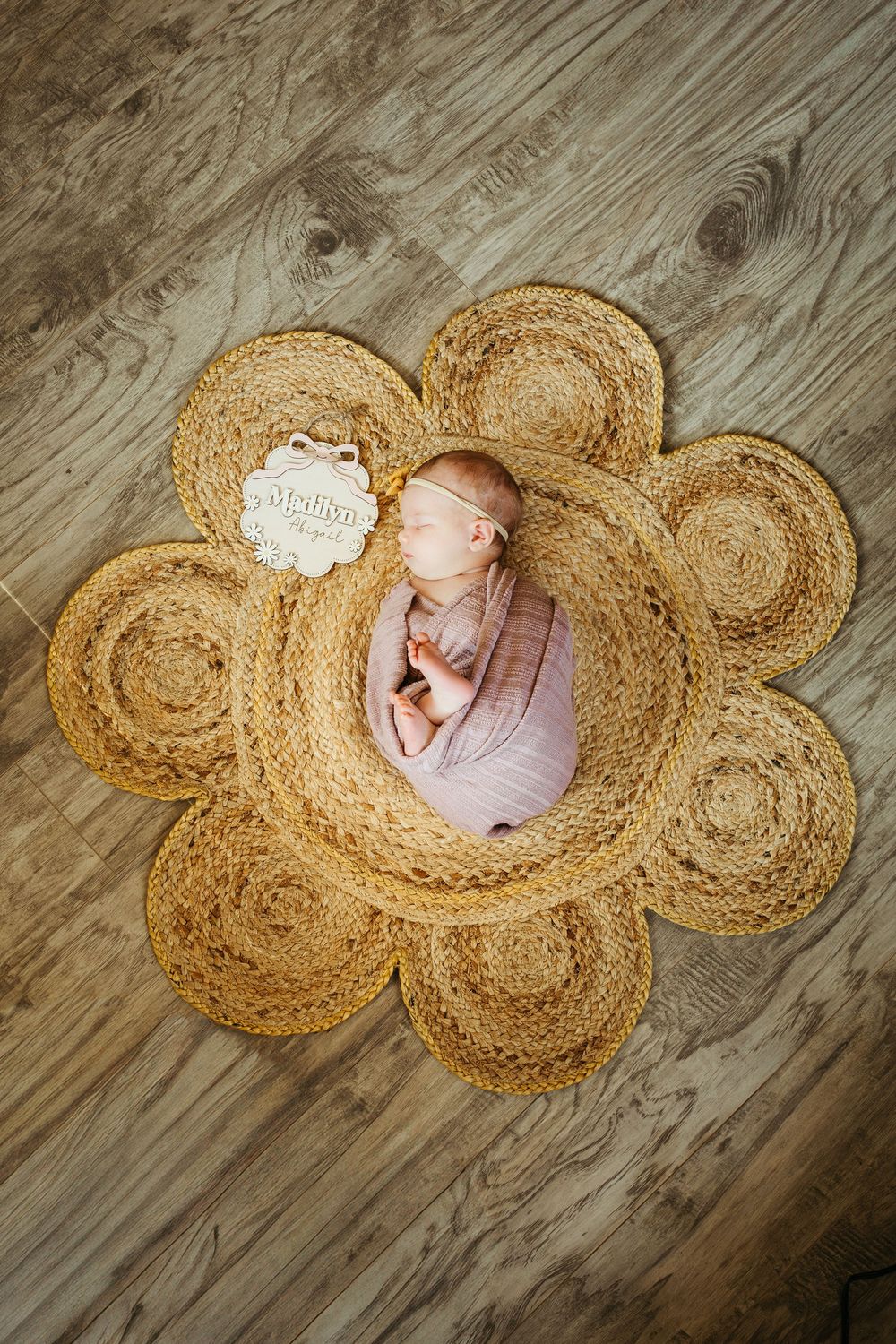 A series of images showing a sleeping newborn nestled in a rustic woven jute rug arranged in a butterfly shape on wooden floor.