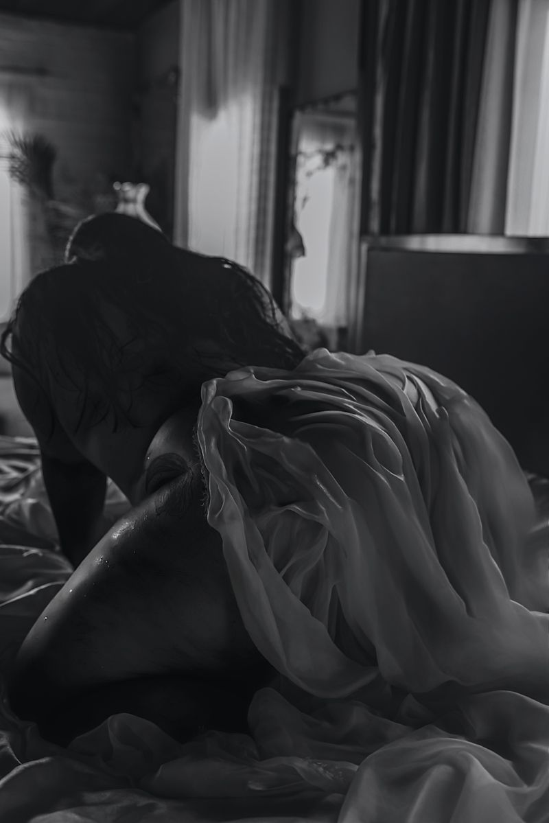 Black and white intimate bedroom scene with draped sheer fabric and soft moody lighting.