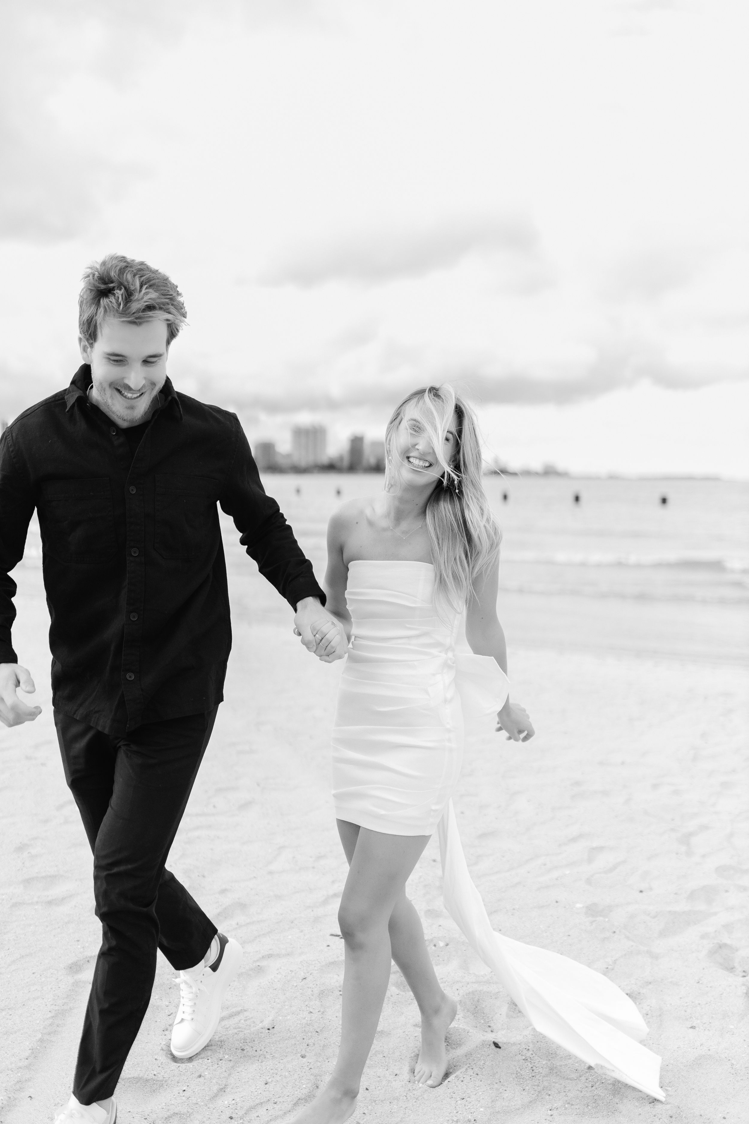 Black and white photo of couple walking joyfully along Chicago's beach.