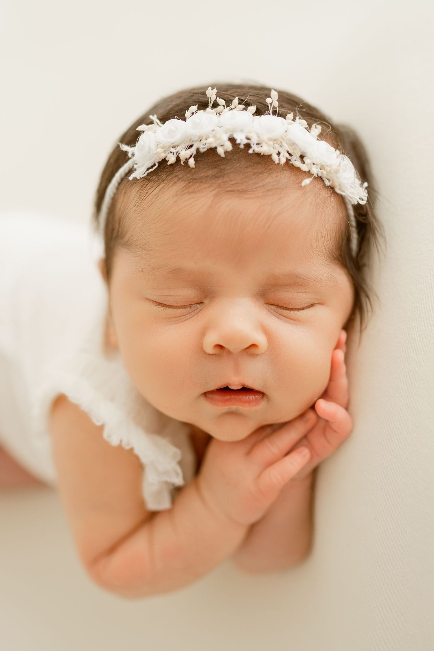 Peaceful sleeping newborn wearing delicate white lace headband in soft natural lighting.