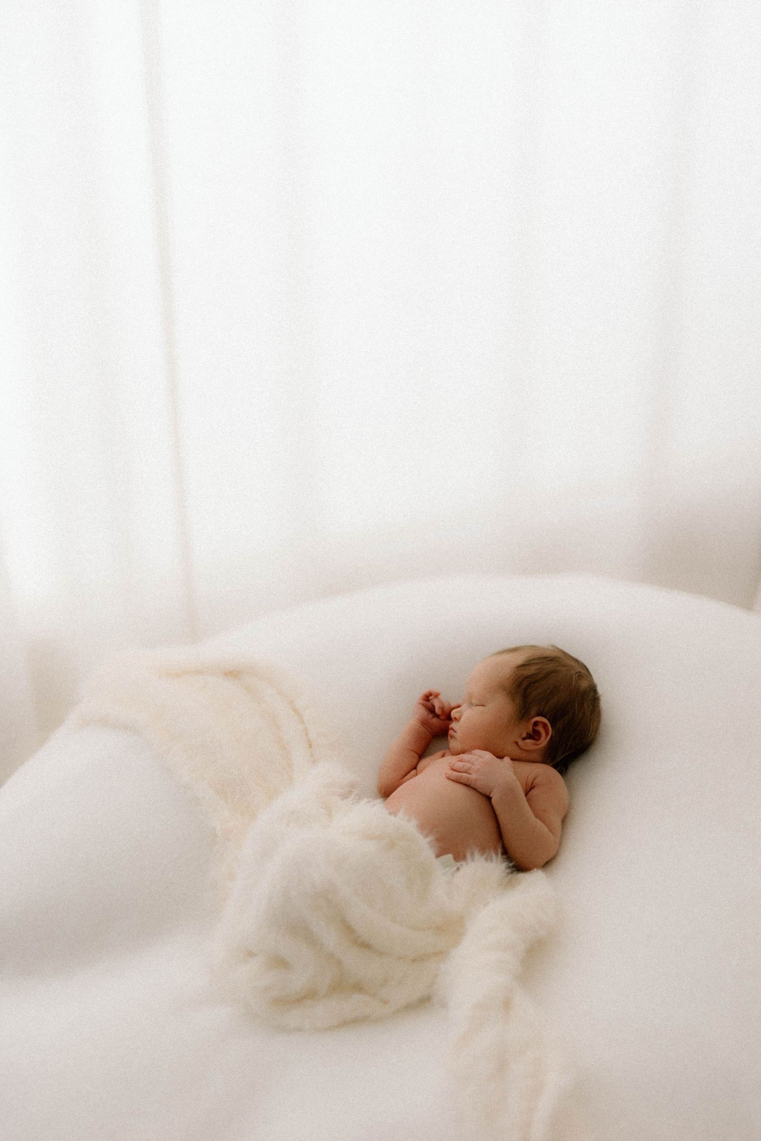 A peaceful sleeping baby wrapped in soft white fabric on a bright white background.