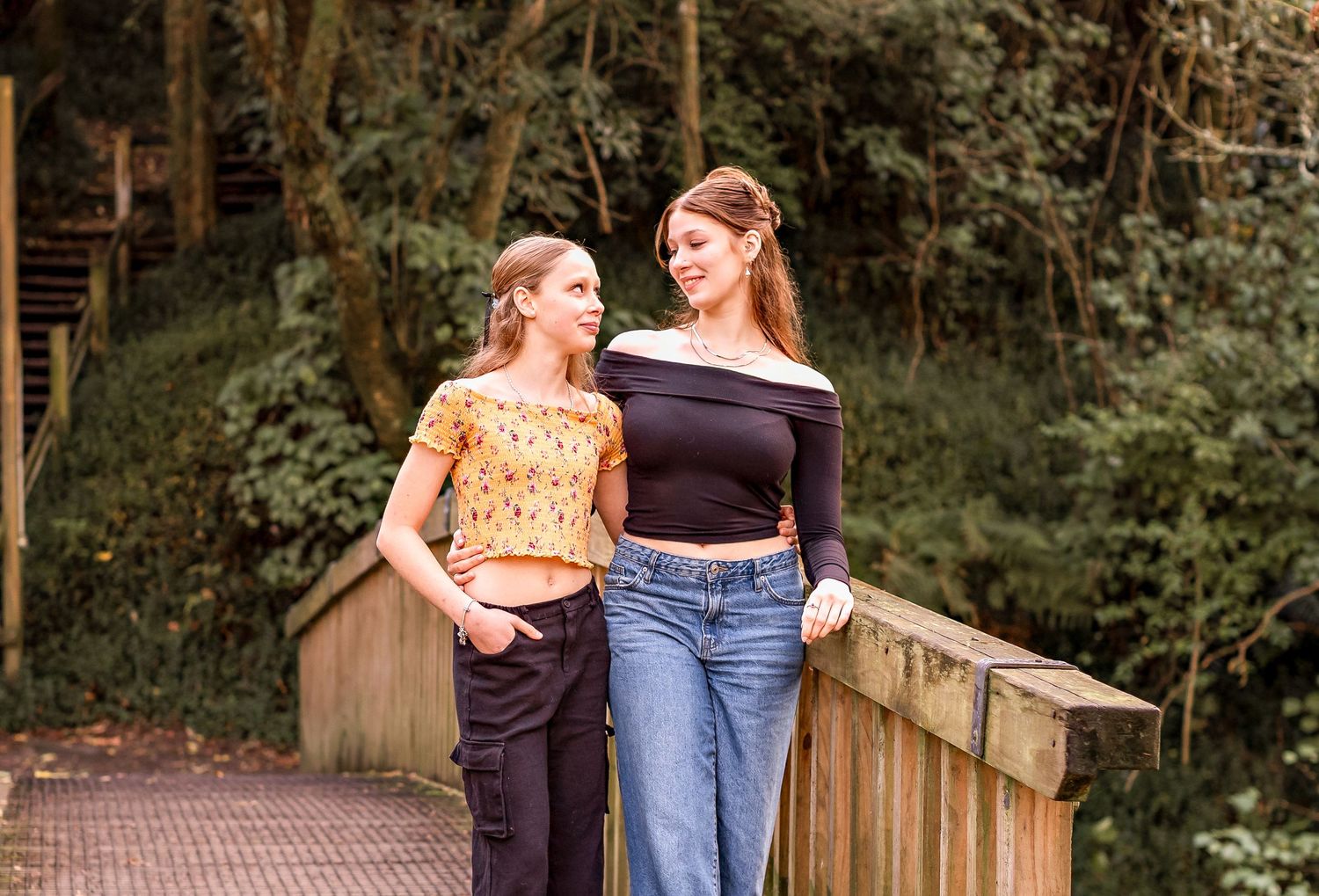 Two sisters walk together on a wooden boardwalk surrounded by lush green forest scenery. Bledisloe Park Palmerston North
