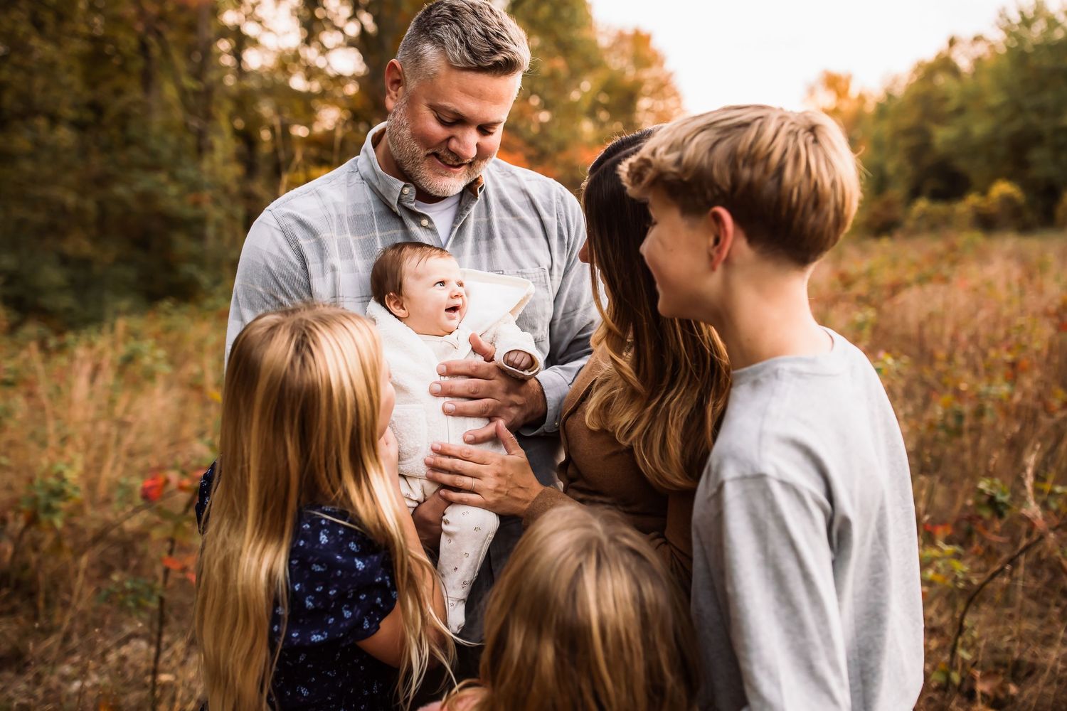A family enjoys a warm autumn evening together in a sunlit field with tall grass and trees.