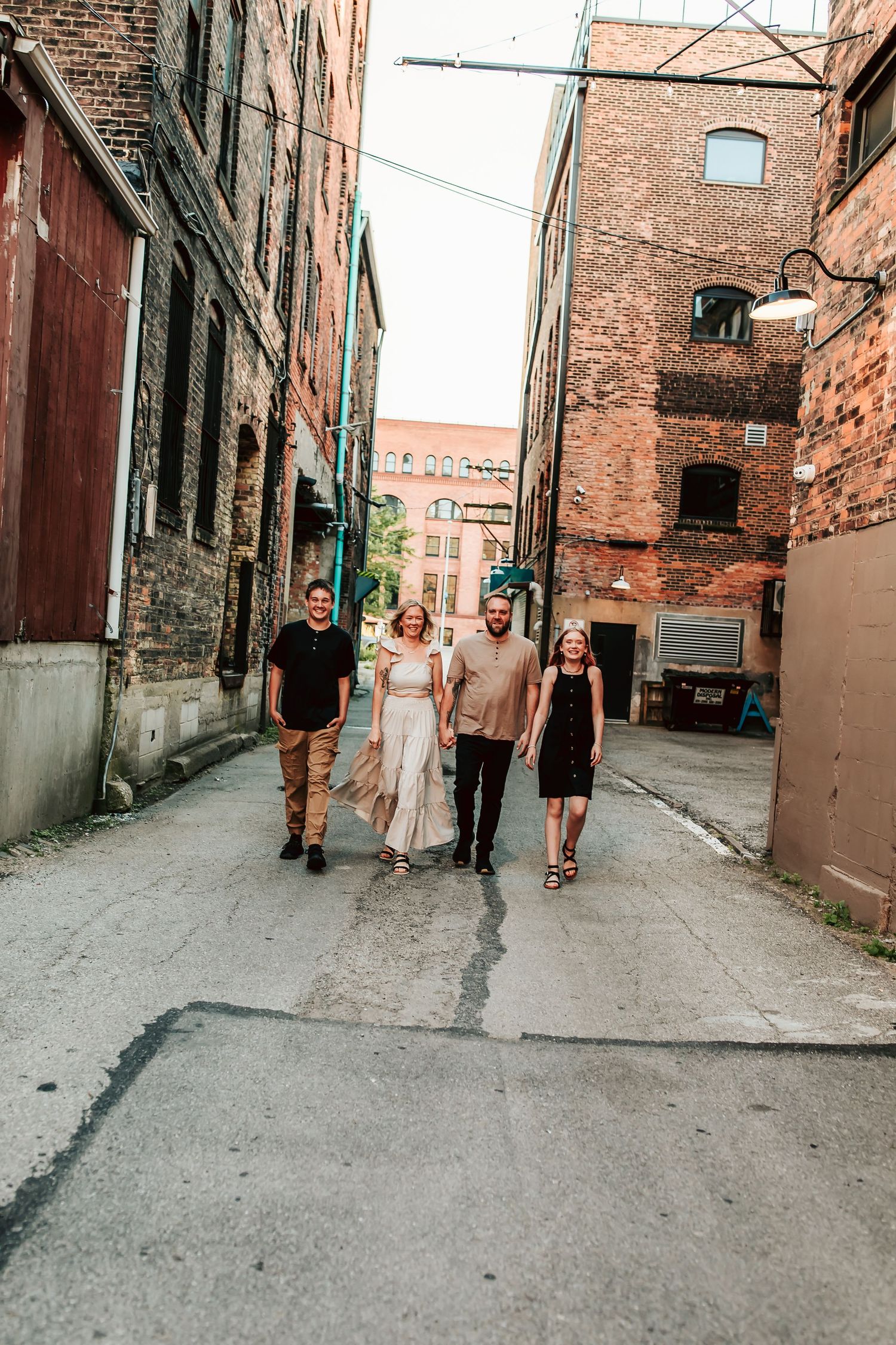 Family walking down narrow urban alley with rustic brick walls and industrial architecture in background.