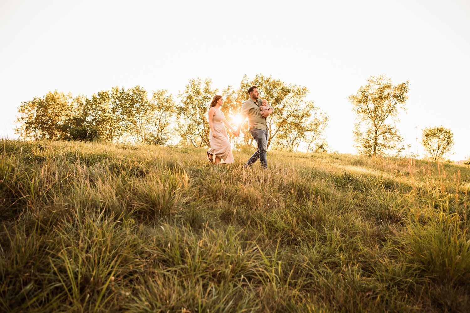 Two silhouetted figures stand on a grassy hill against a glowing golden sunset.
