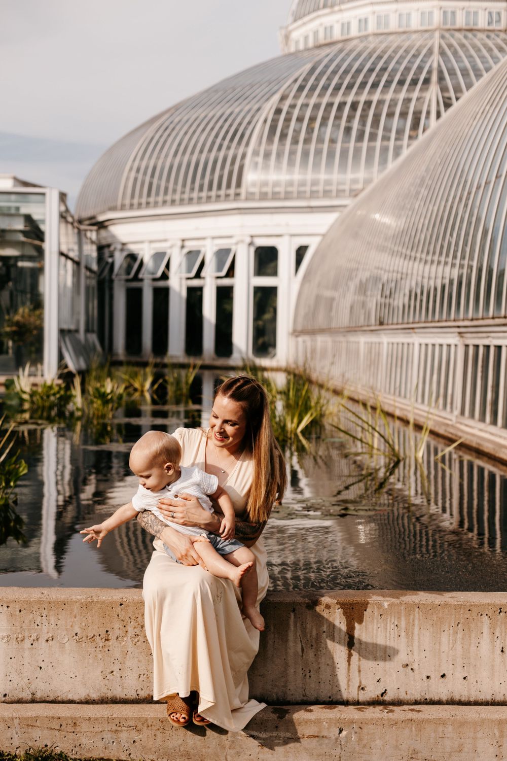 Parent and baby sitting by ornate greenhouse dome at botanical gardens.