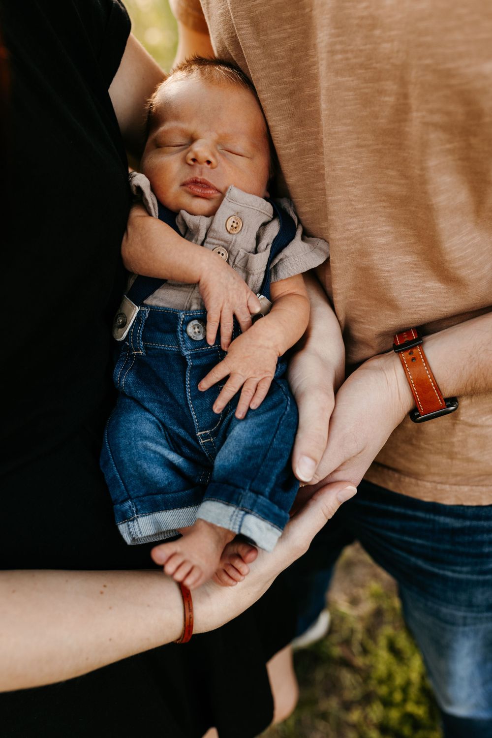 Sleeping baby nestled between parents wearing denim and casual clothing.
