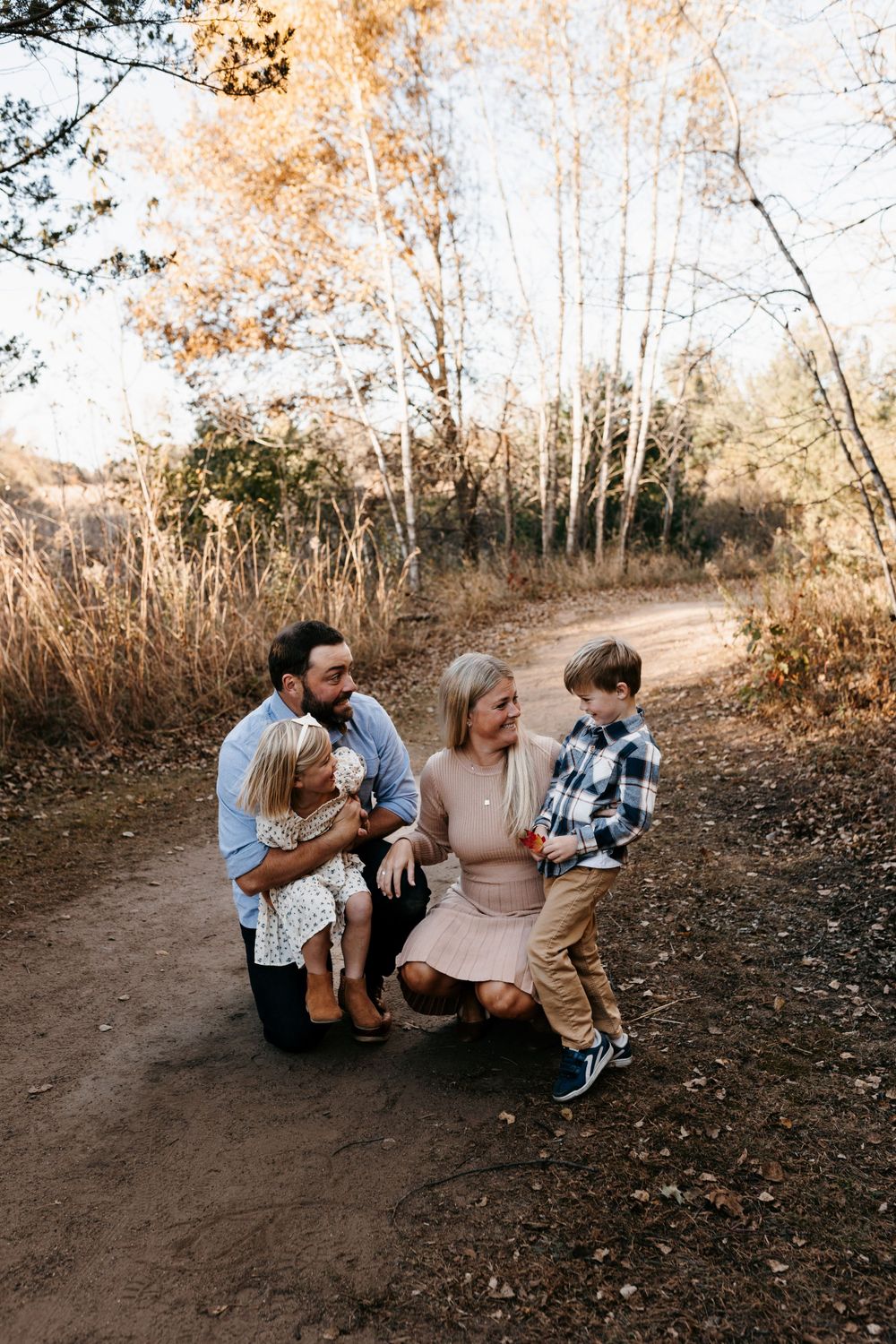 A family group kneeling together on a dirt path surrounded by autumn trees.