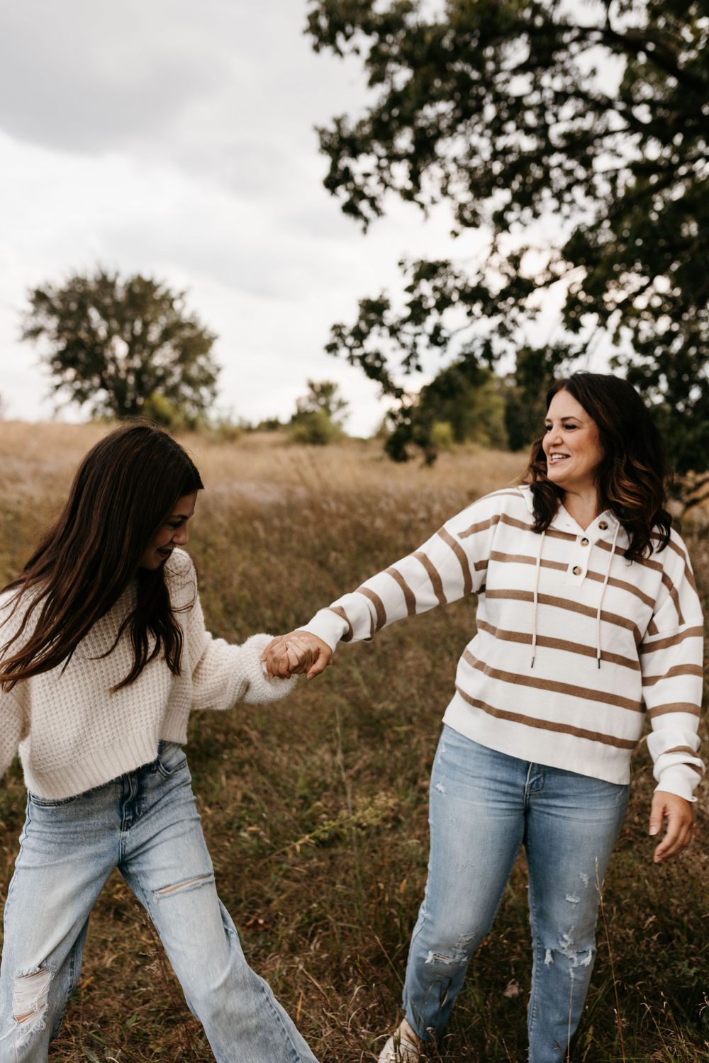 Two people in matching sweaters hold hands while enjoying a playful moment outdoors.