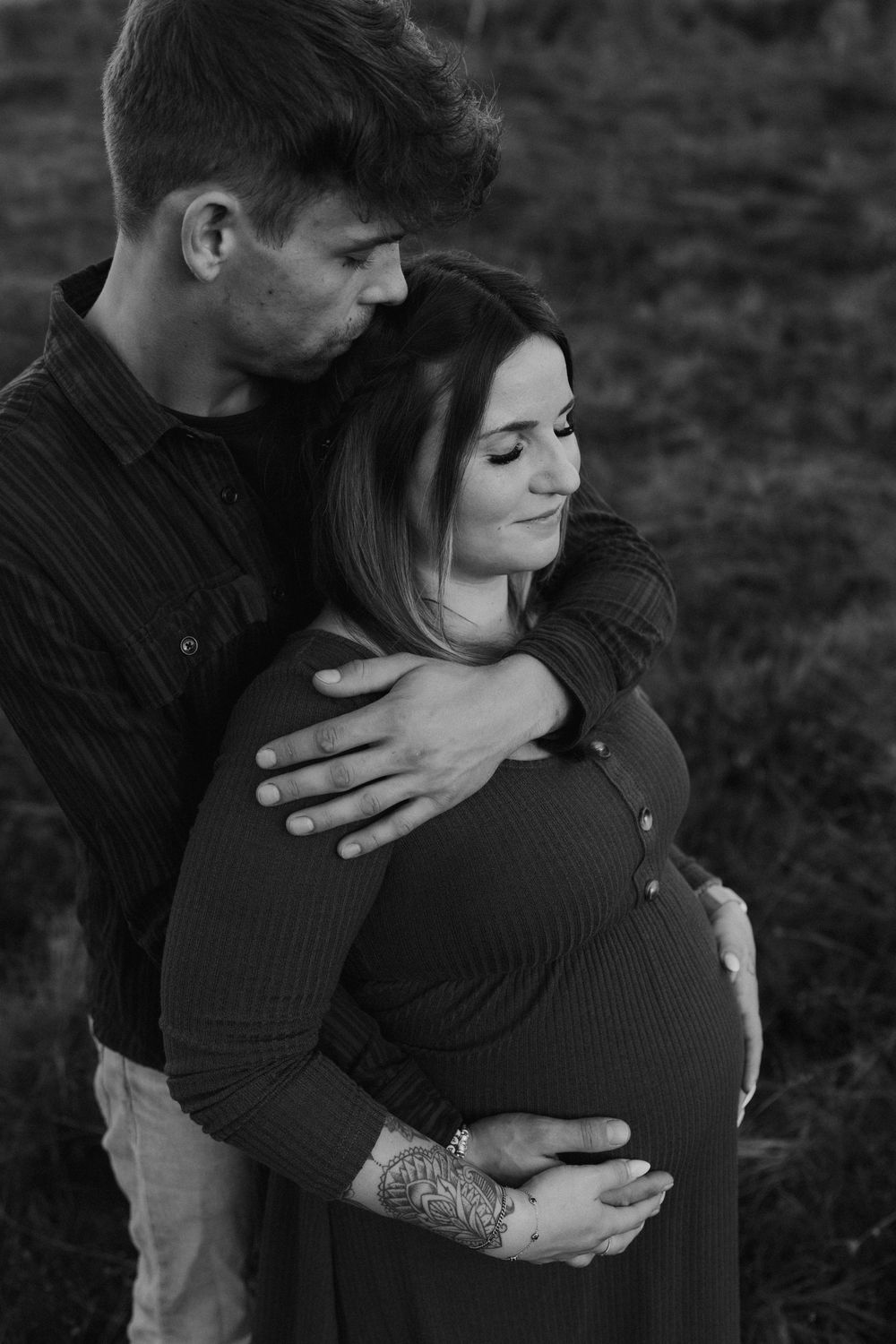 Partner umarmt die schwangere Frau von hinten und hält sanft ihren Babybauch, ruhige Momentaufnahme