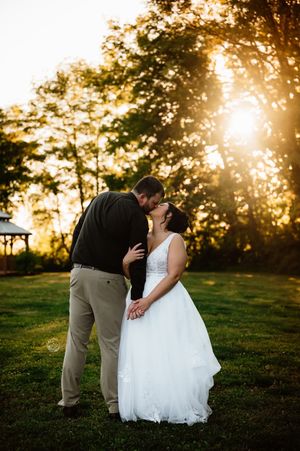 Bride and groom share a romantic kiss at golden sunset in a lush green outdoor wedding venue.
