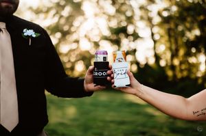 Bride and groom toasting with custom wedding koozies outdoors at golden hour.