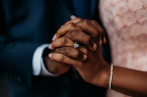 Couple holding hands with a diamond engagement ring, wearing formal attire in a romantic close-up wedding photo.