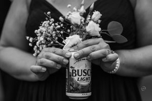A bridesmaid holds a Busch Light beer can adorned with a floral bouquet at a wedding reception.