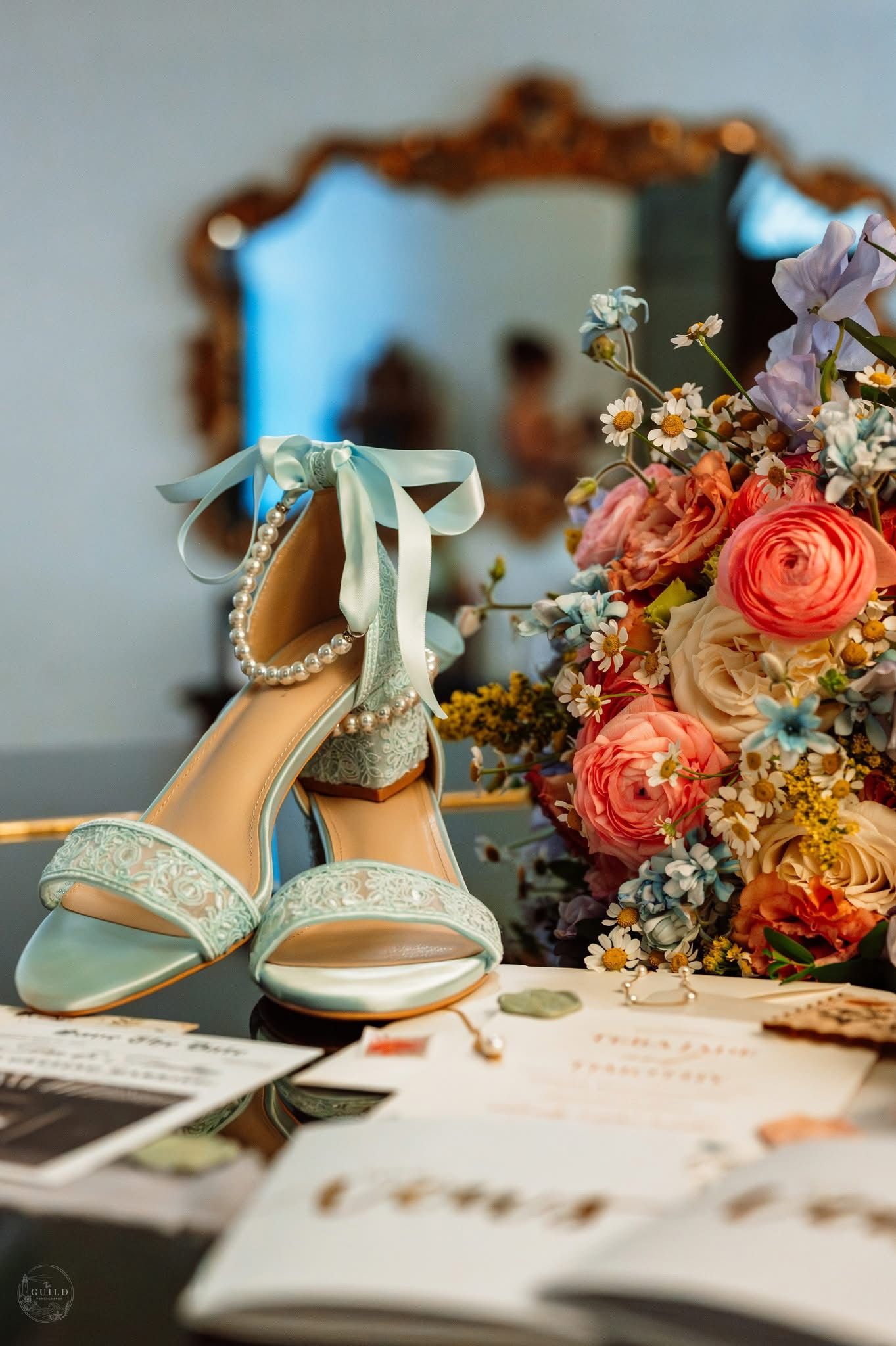 Light blue pearl-embellished bridal heels with ribbon ties displayed beside a colorful floral bouquet.
